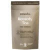 Amoda Remedy Tea steeped in a ceramic cup with visible organic herbs like ginger, elderberries, and star anise beside a pouch of loose-leaf blend
