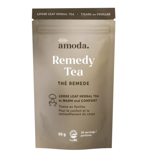 Amoda Remedy Tea steeped in a ceramic cup with visible organic herbs like ginger, elderberries, and star anise beside a pouch of loose-leaf blend